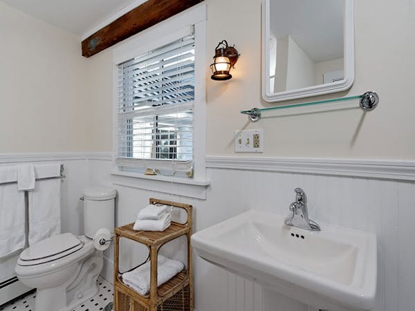 Bathroom of America's Cup room -- very clean, white, with a pedestal sink and exposed beams.