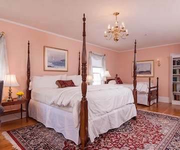 Four-post, king-sized bed in foreground, twin-sized bed in background, beautiful chandelier hanging in center of room.
