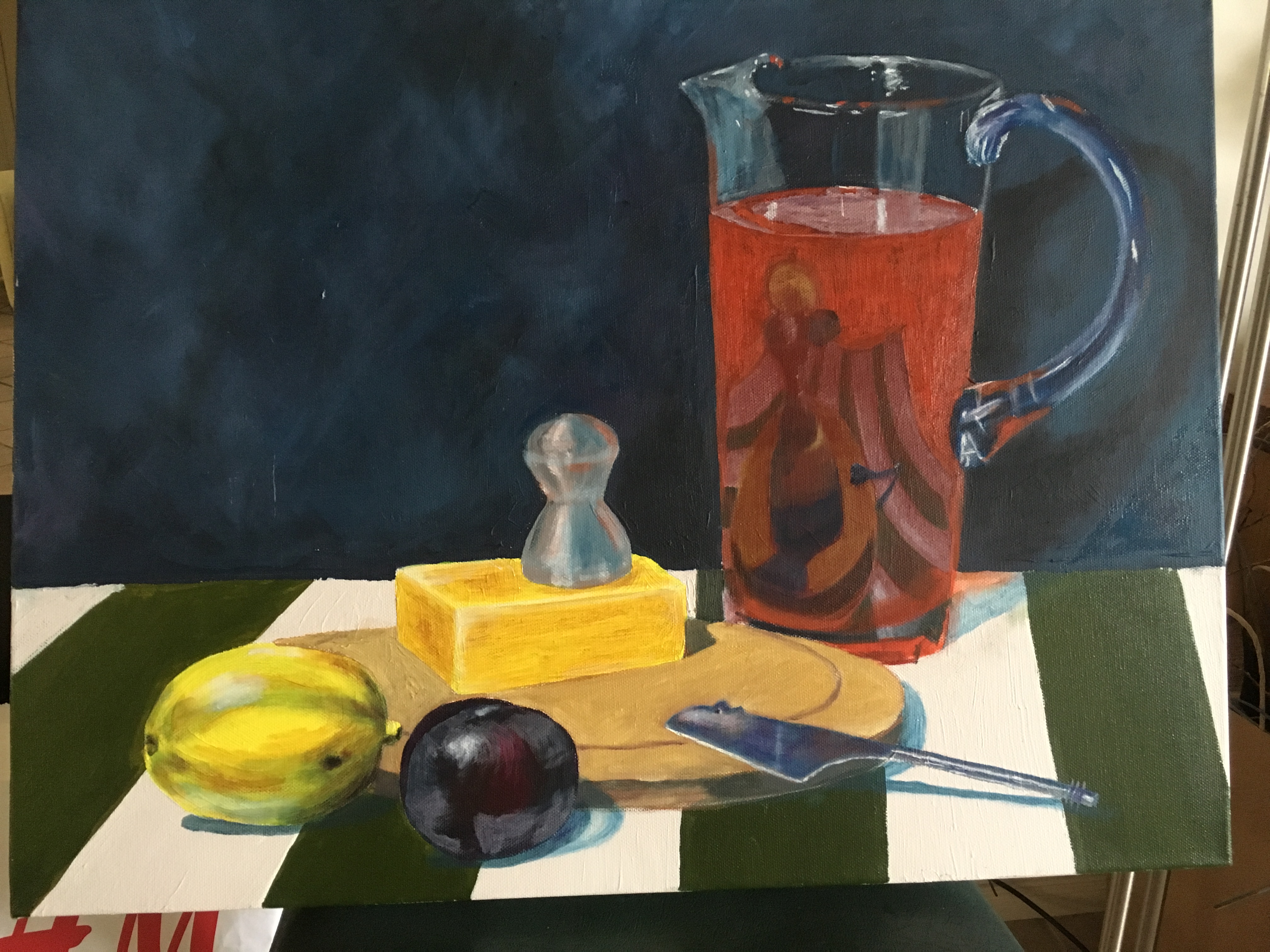 Detail of a painted still life, with cheese, fruits and a jug on a green and white striped tablecloth.