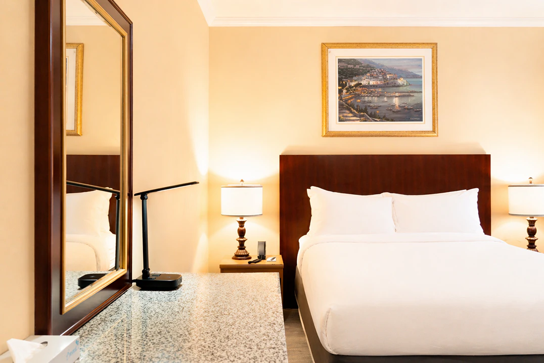 A hotel room with a large bed, two nightstands with lamps, a mirror, and artwork on the wall.