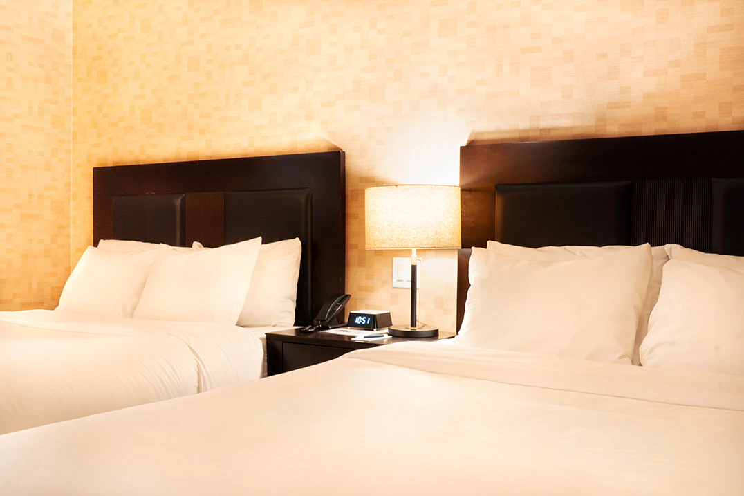 A hotel room with two queen beds, dark wood headboards, and white bedding.
