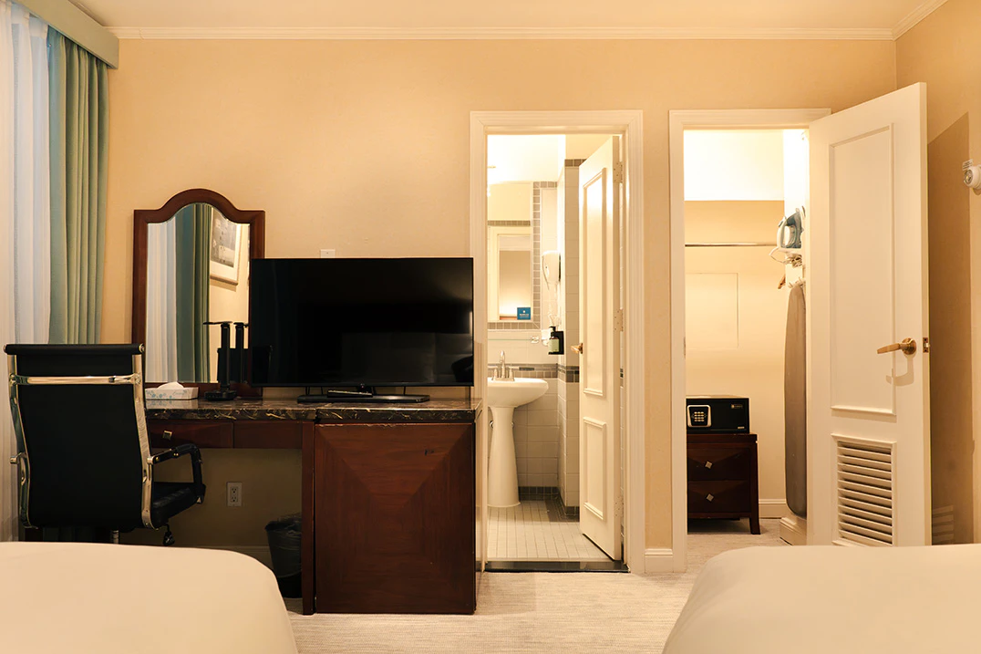 A hotel room with a desk, TV, and mirror, with a bathroom and closet in the background.