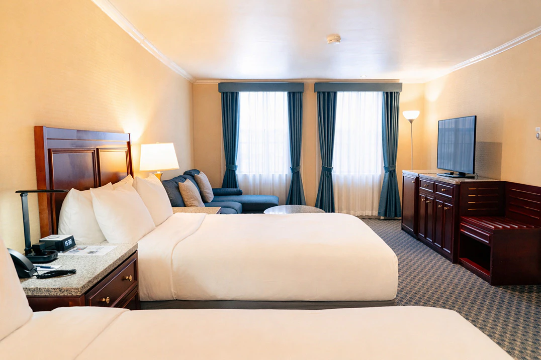 A wide view of a hotel room with two beds, a TV, and a seating area.