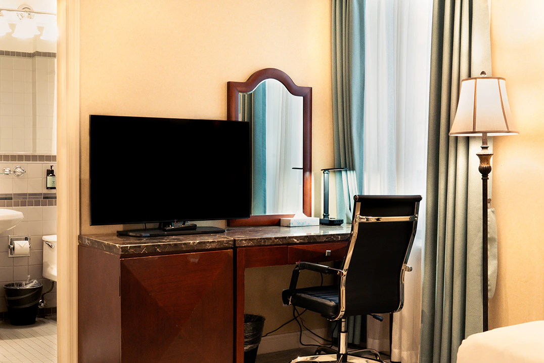 A hotel room with a desk, TV, and chair.