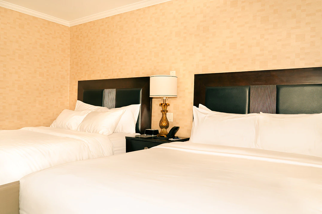 A hotel room with two queen beds, dark wood headboards, and white bedding.