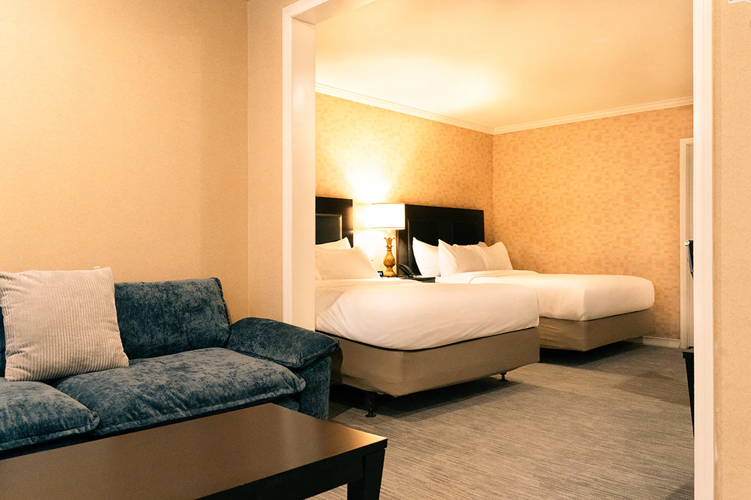 A hotel room with a sofa, two beds, and a lamp.