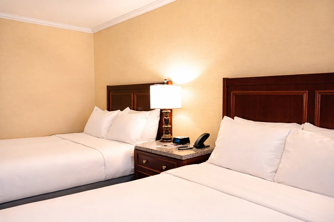 A hotel room with two beds, dark wood headboards, and a nightstand with a lamp and telephone.