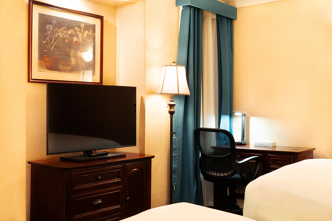 A hotel room with a TV, desk, lamp, and bed