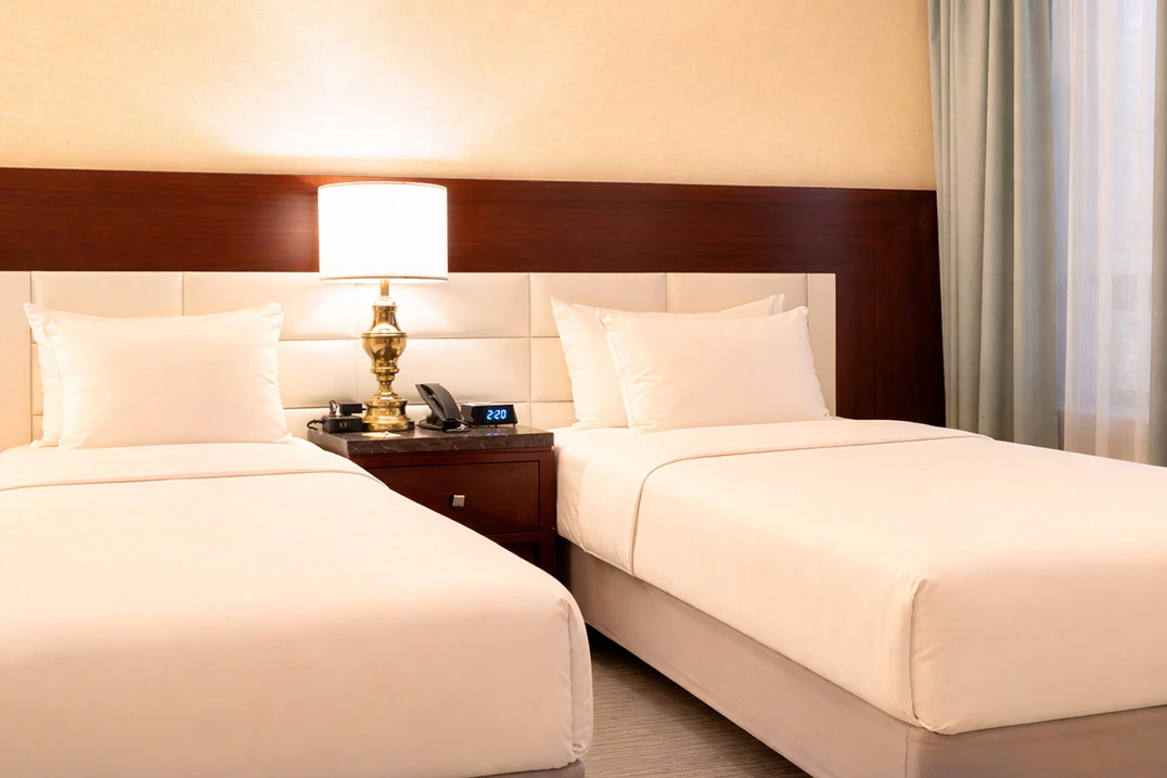 A hotel room with two twin beds, a nightstand, and a lamp.