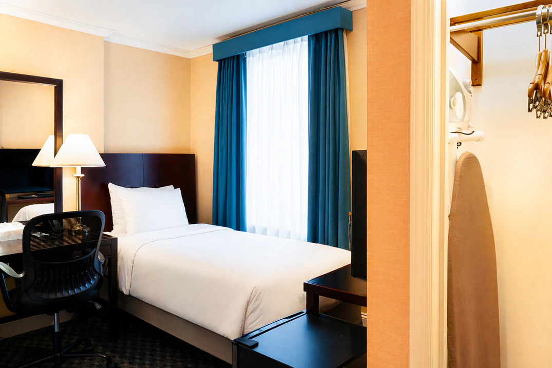 A hotel room with a bed, desk, and window