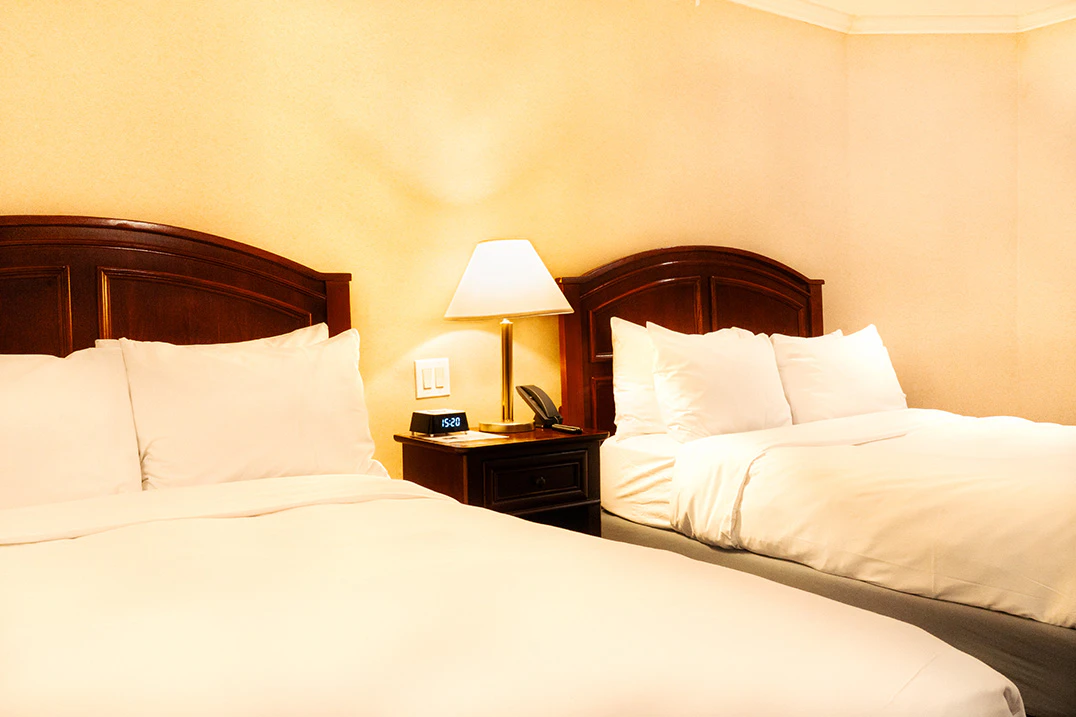 A hotel room with two twin beds, wooden headboards, and a nightstand with a lamp.