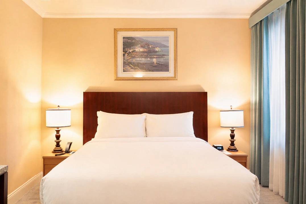 A hotel room with a large bed, two nightstands with lamps, and a painting above the headboard.