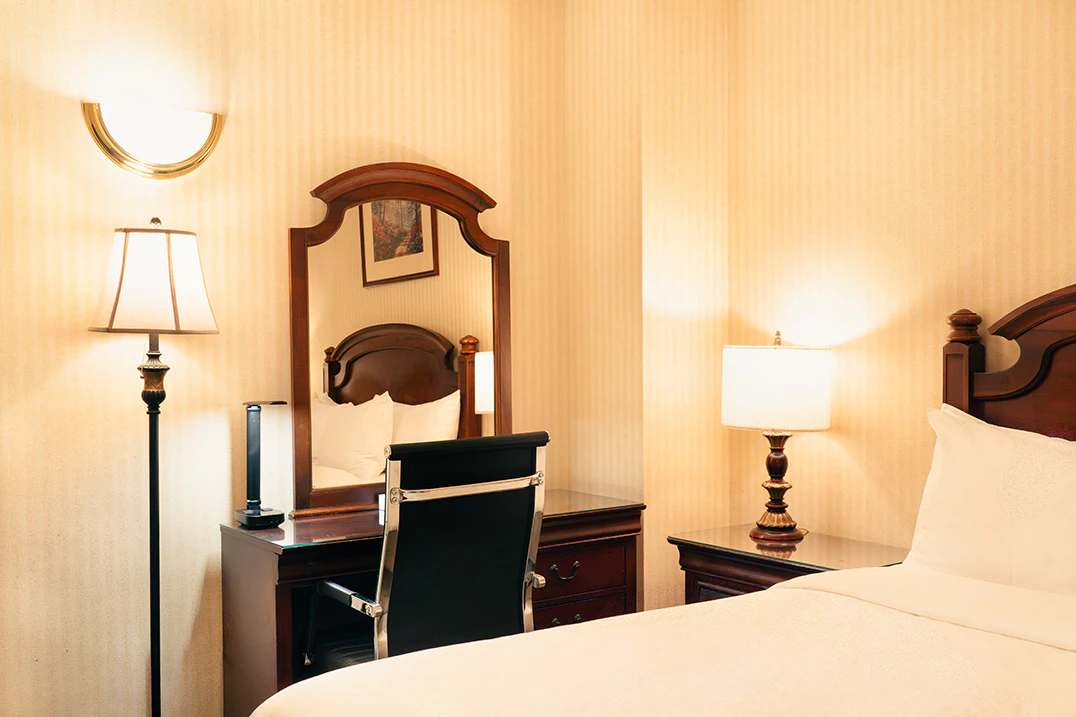 A hotel room with a queen bed, dresser, mirror, and lamp.