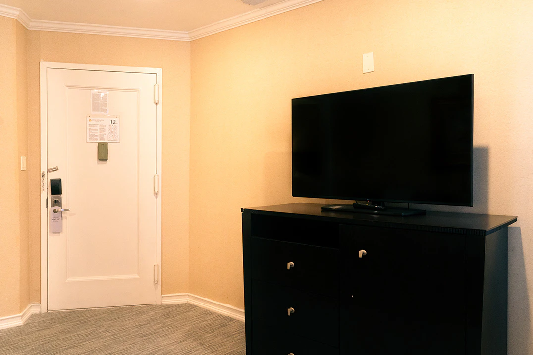 A hotel room with a black dresser, flat-screen TV, and a door with a sign.