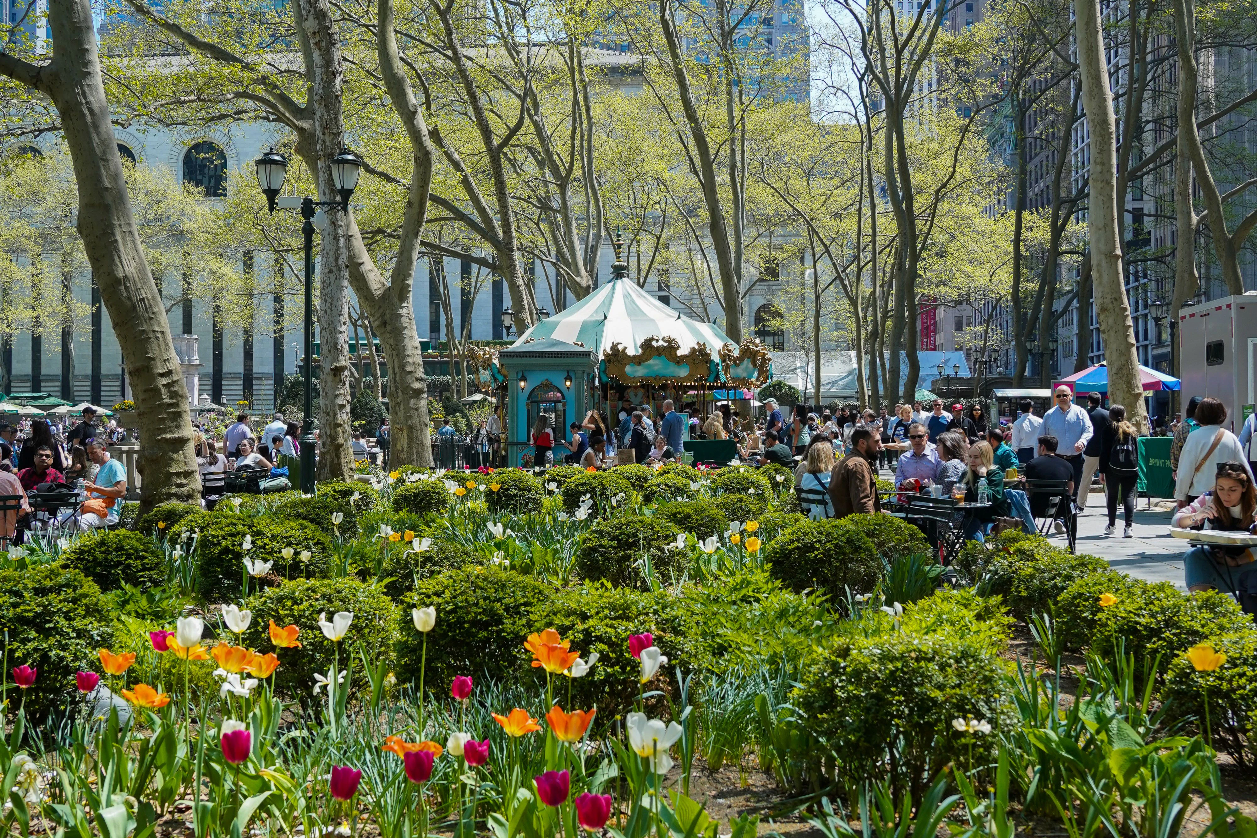 a sunny day in a park with people, flowers, and a carousel