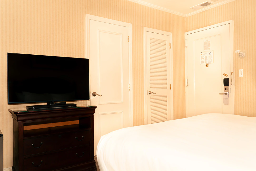 A hotel room with a bed, TV on a dresser, and two doors
