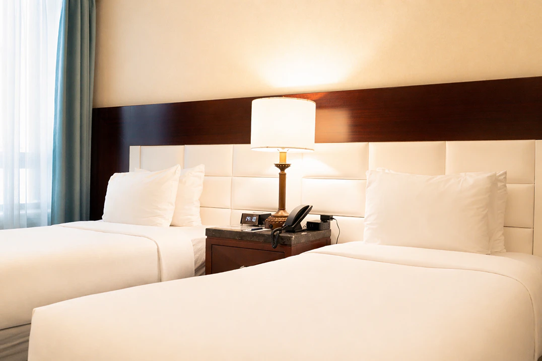 A hotel room with two beds, a nightstand, and a window.