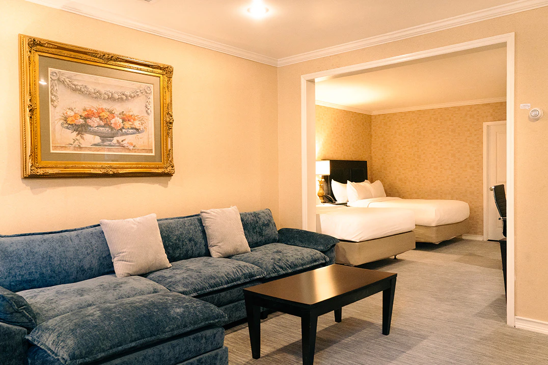A hotel room with a blue sofa, coffee table, and a bed in the background.