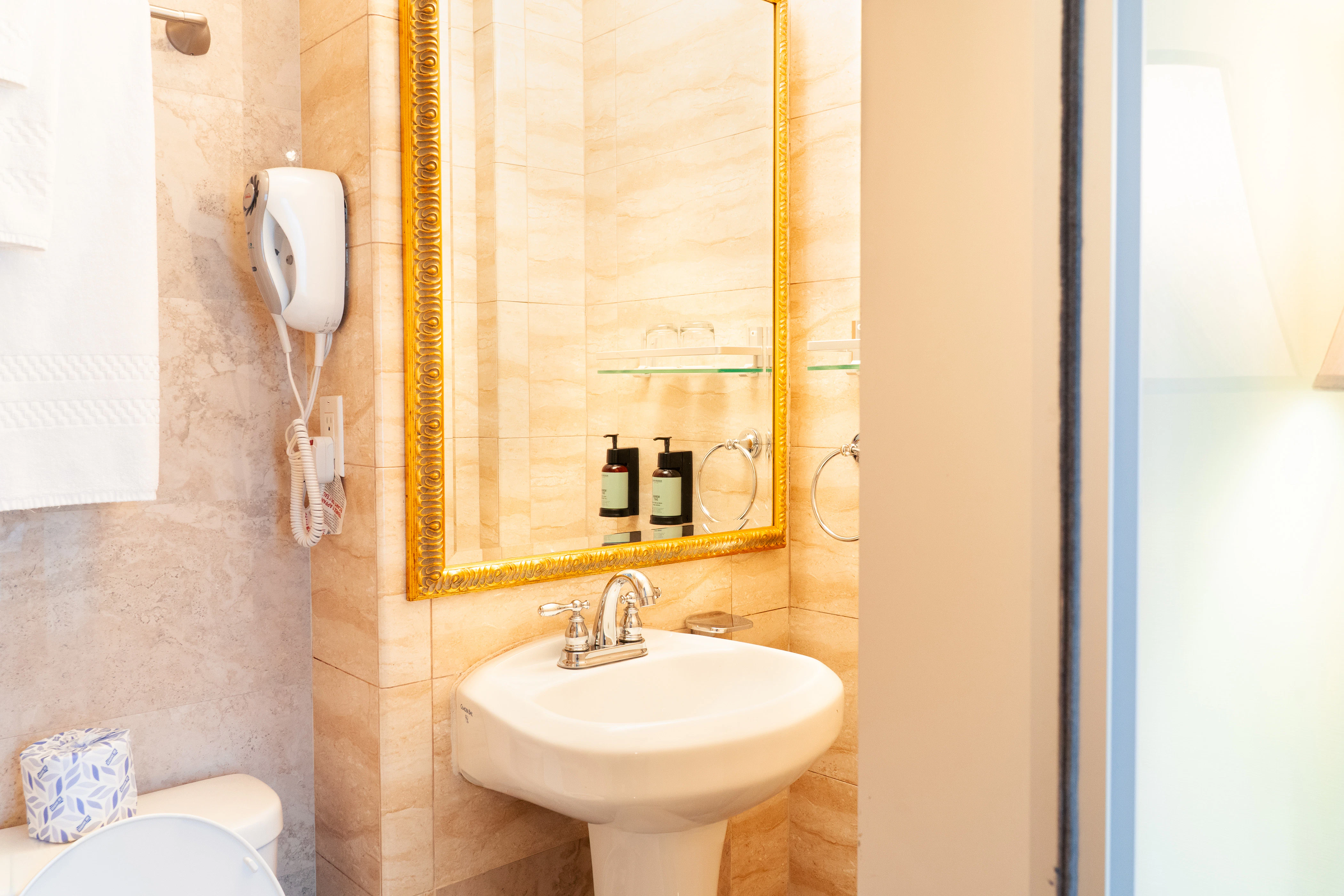 A bathroom with a gold-framed mirror, white sink, and tiled walls.