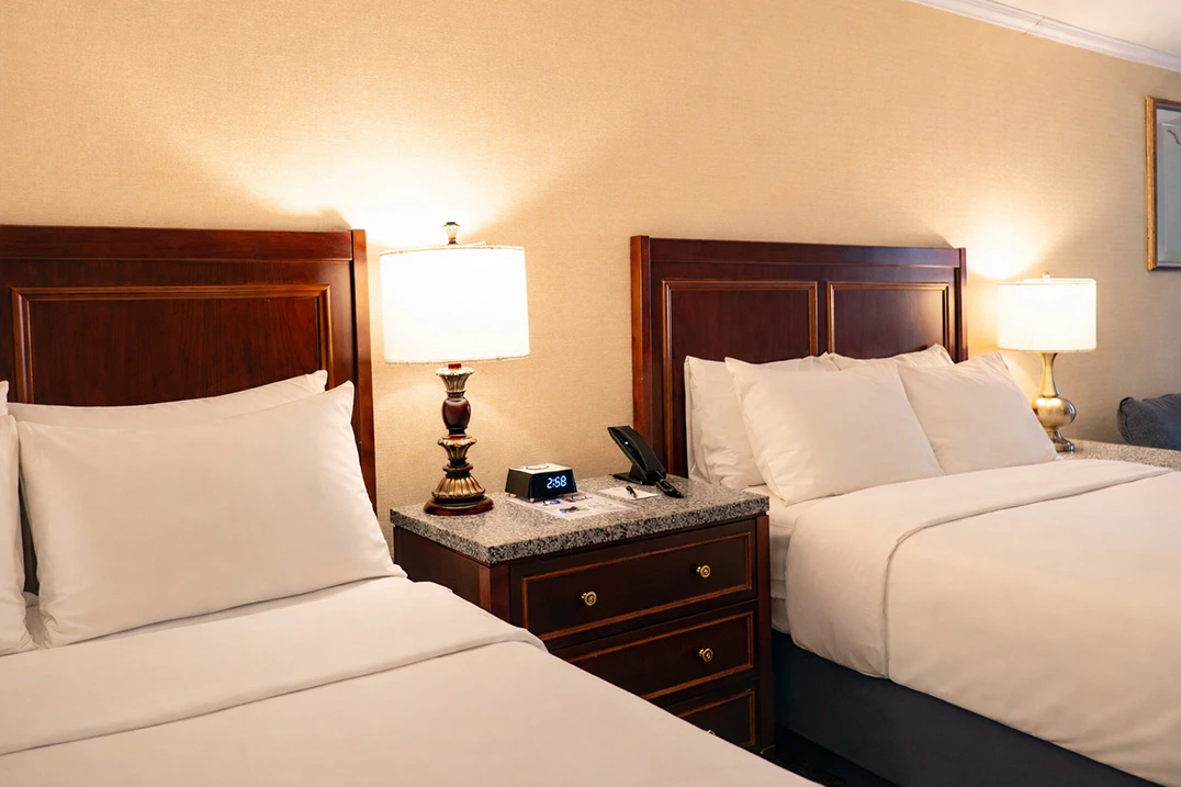 A hotel room with two twin beds, nightstand, and lamps.