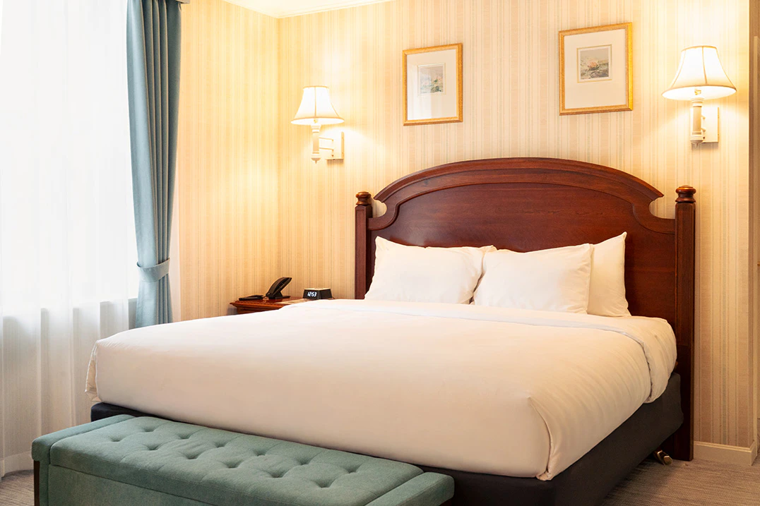 A hotel room with a large bed, green bench, and city view