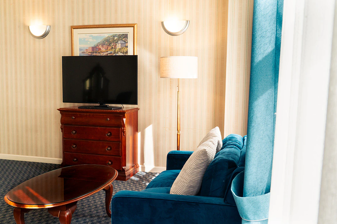 A hotel room with a teal sofa, wooden dresser, flat-screen TV, and lamps.
