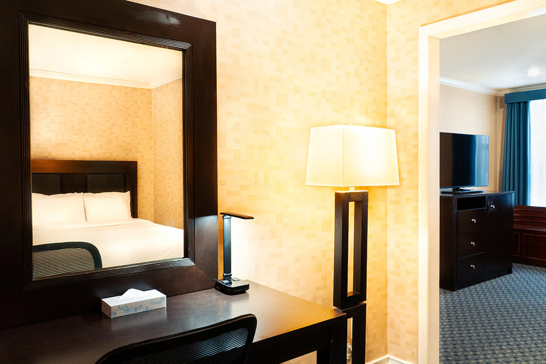 A hotel room with a desk, mirror, and lamp