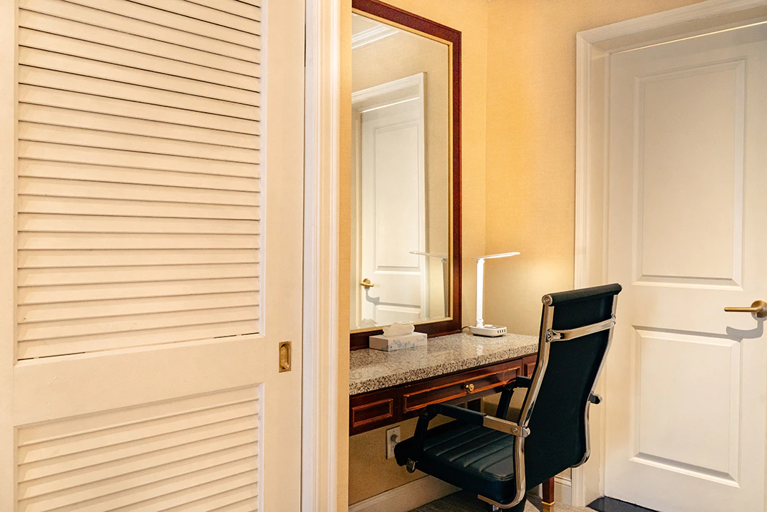 A hotel room with a desk, mirror, and chair.