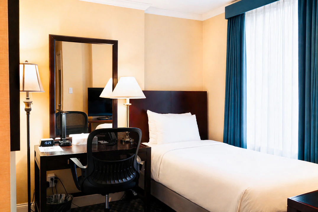 A hotel room with a single bed, desk, chair, and window.