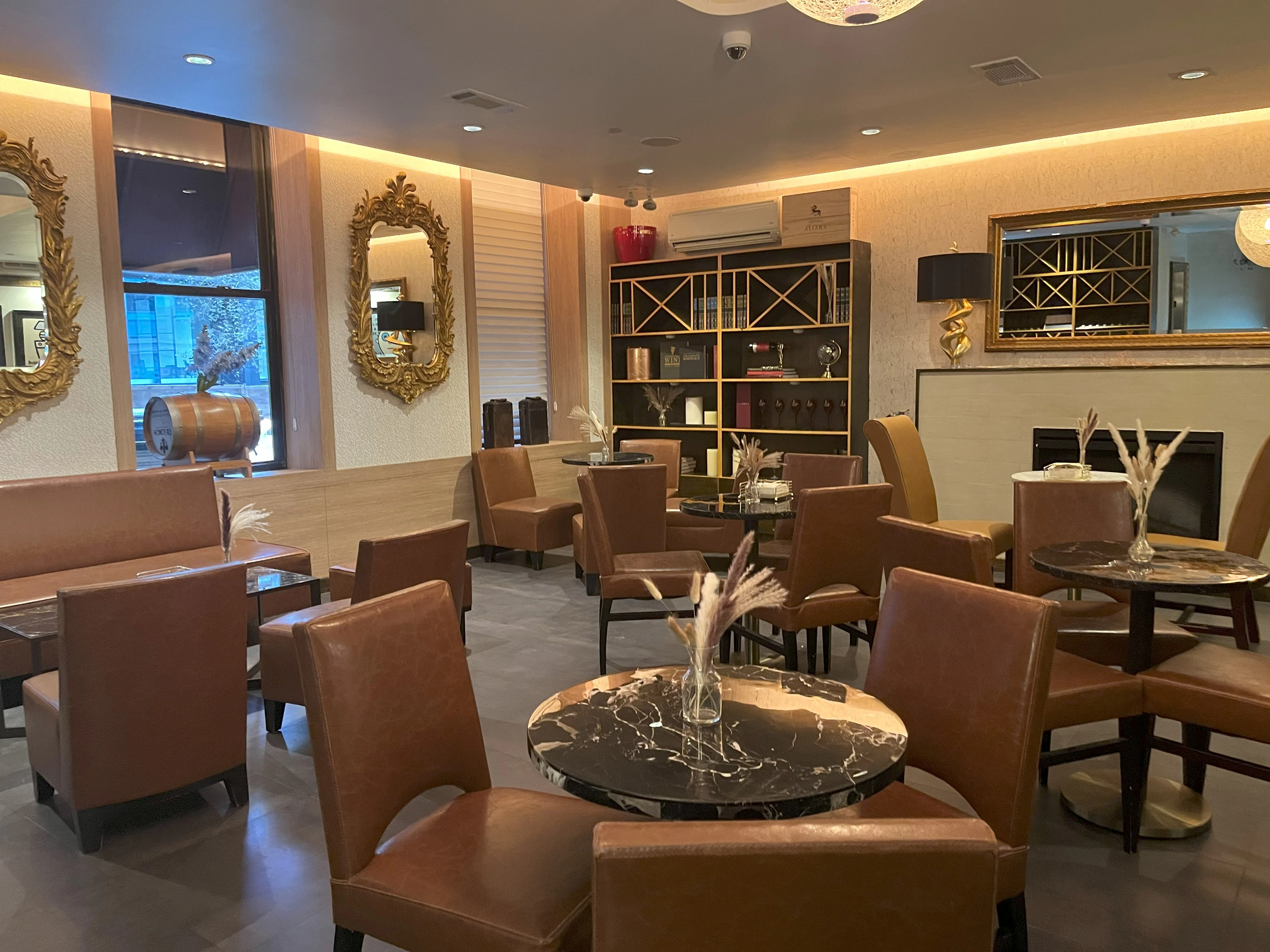 A luxurious lounge with brown leather chairs, marble tables, and gold mirrors.
