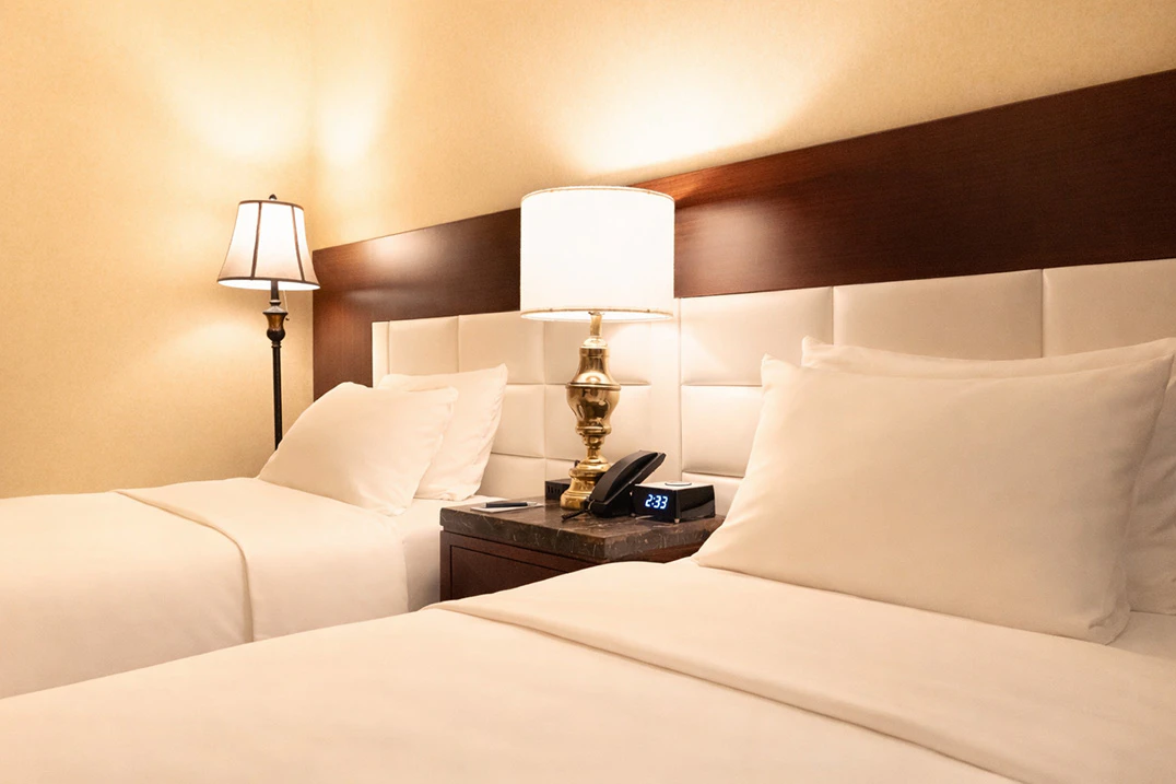 A hotel room with two twin beds, a nightstand with a lamp and phone, and a padded headboard.