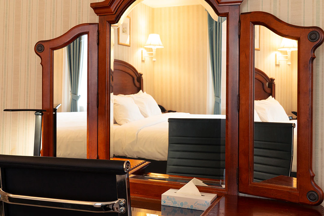 A hotel room with a large mirror, a bed, and a chair.