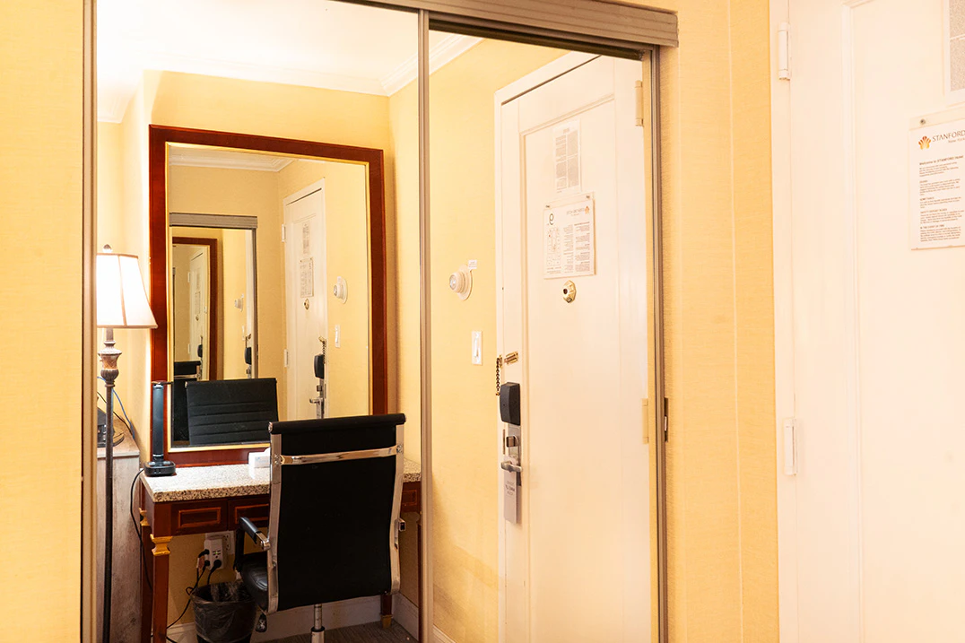 A hotel room with a desk, mirror, and door.