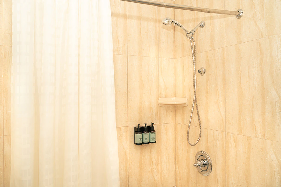 A shower with a white curtain, tan tile, and bottles of soap