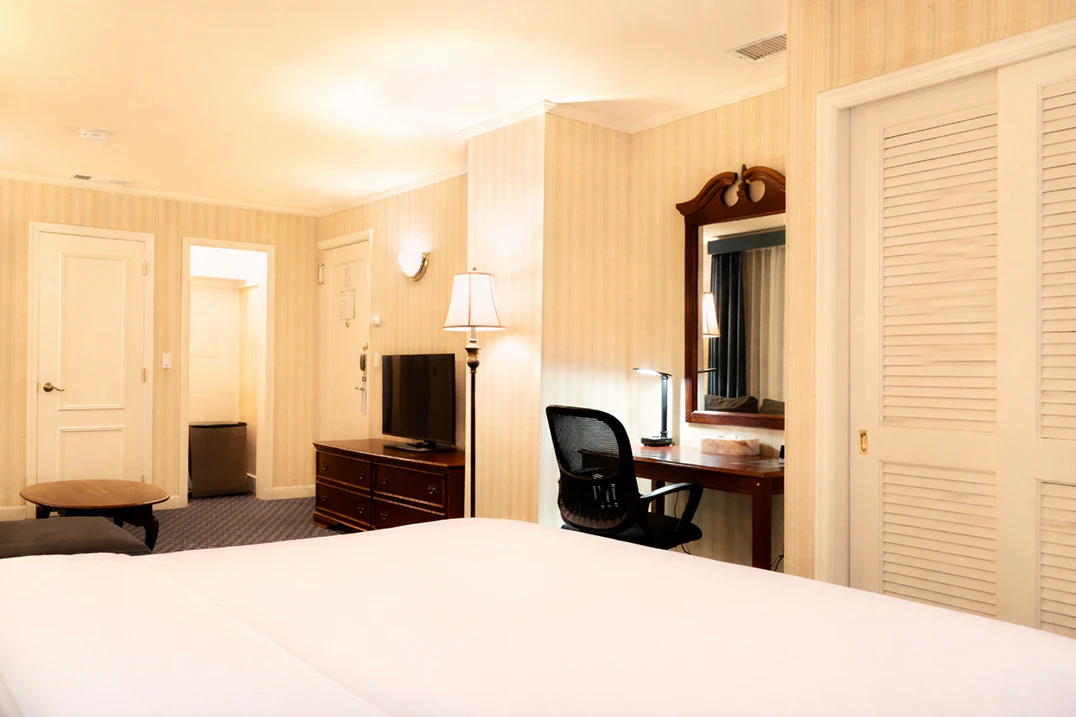 A wide view of a hotel room with a king bed, desk, TV, and closet.