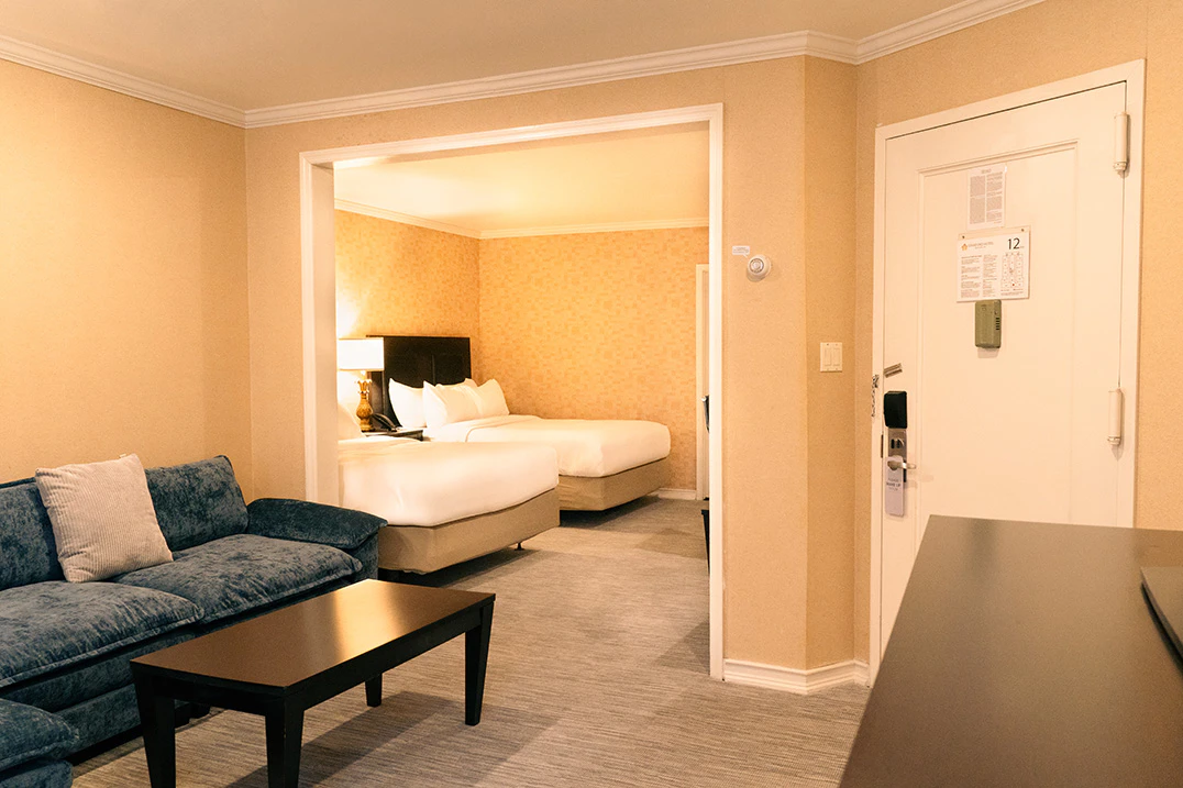 A hotel room with a sofa, coffee table, two queen beds, and an open door