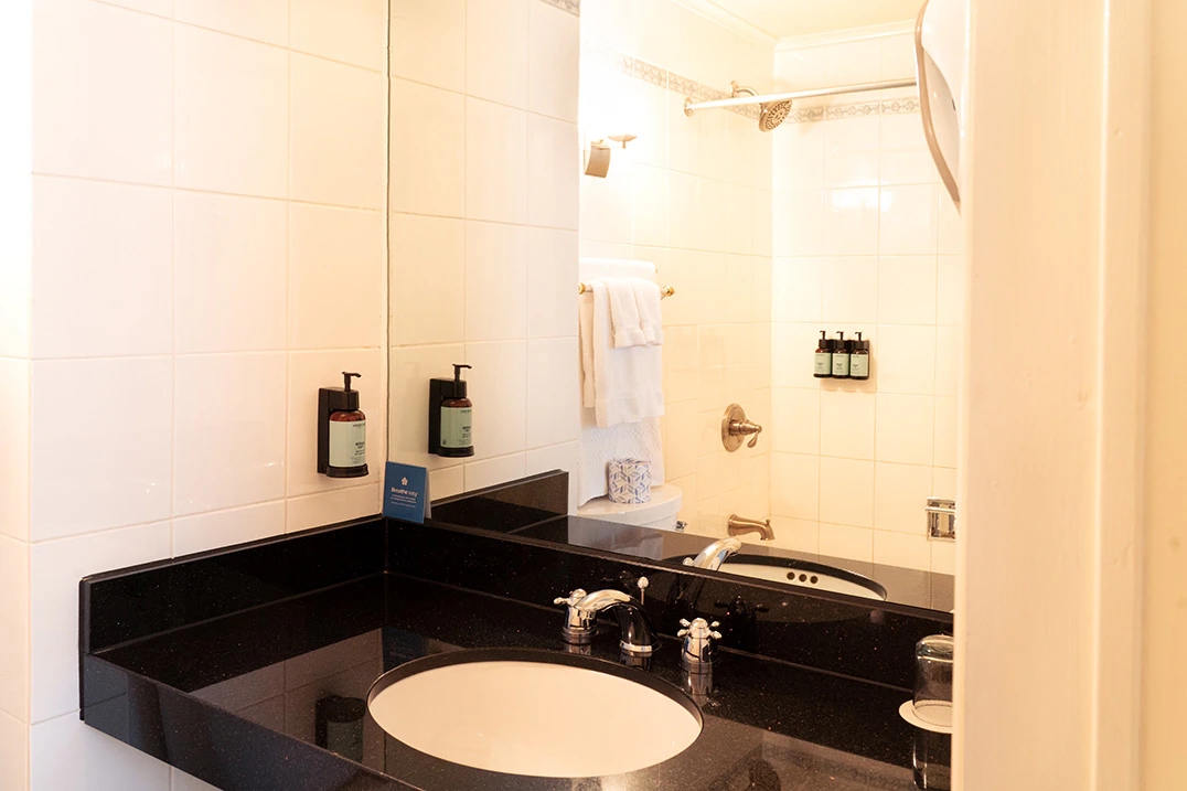 A bathroom with a black countertop, white sink, and mirror reflecting the shower