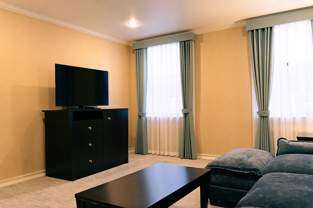A hotel room's living area with a TV, dresser, sofa, and coffee table.