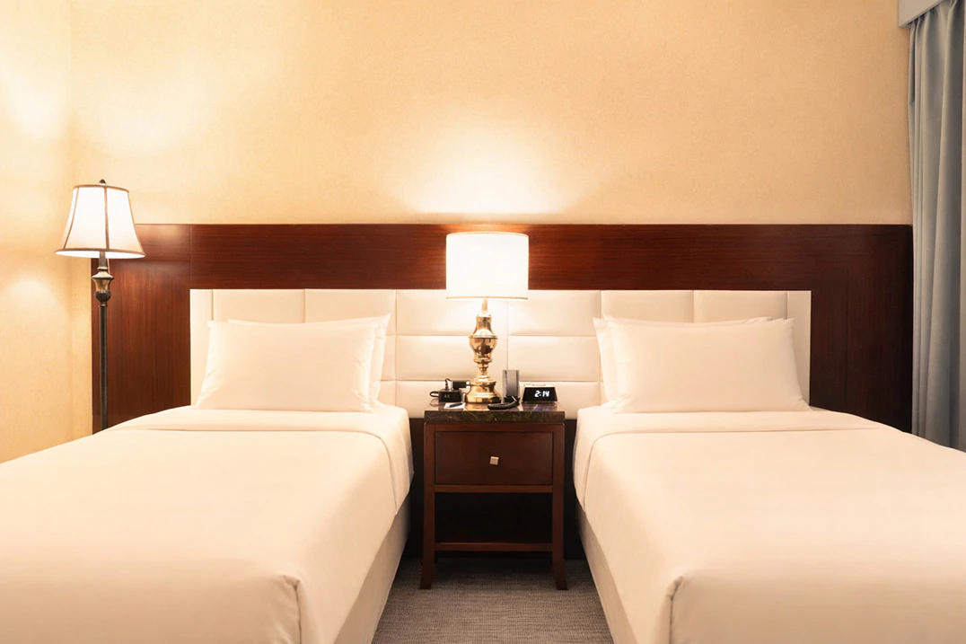 A hotel room with two twin beds, a nightstand, and lamps.