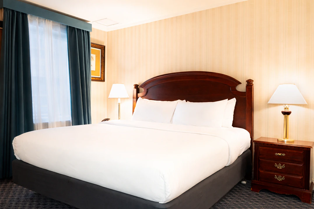 A hotel room with a large bed, two nightstands with lamps, and a window with curtains.