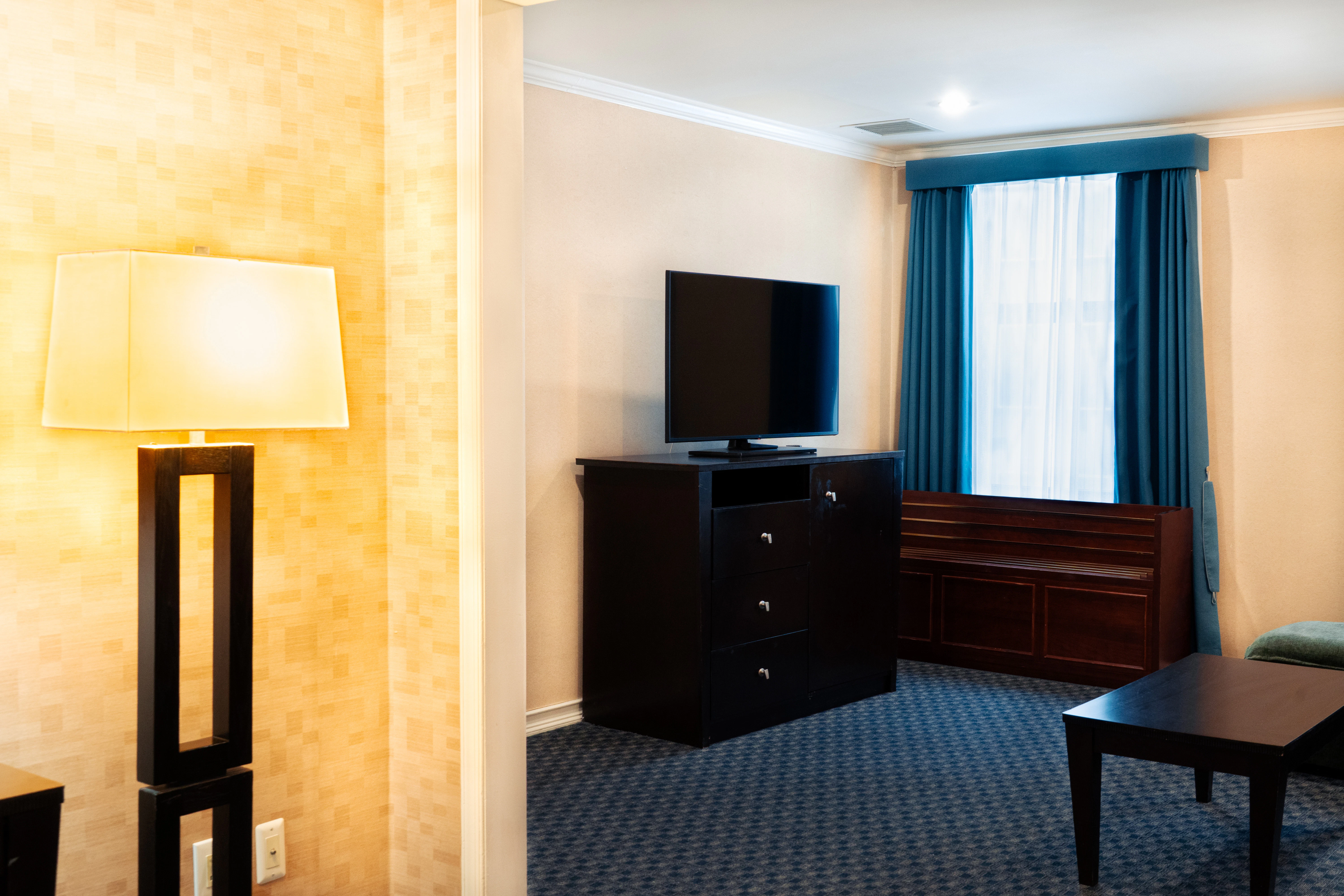 A wide view of a hotel room with a TV, dresser, lamp, and window.