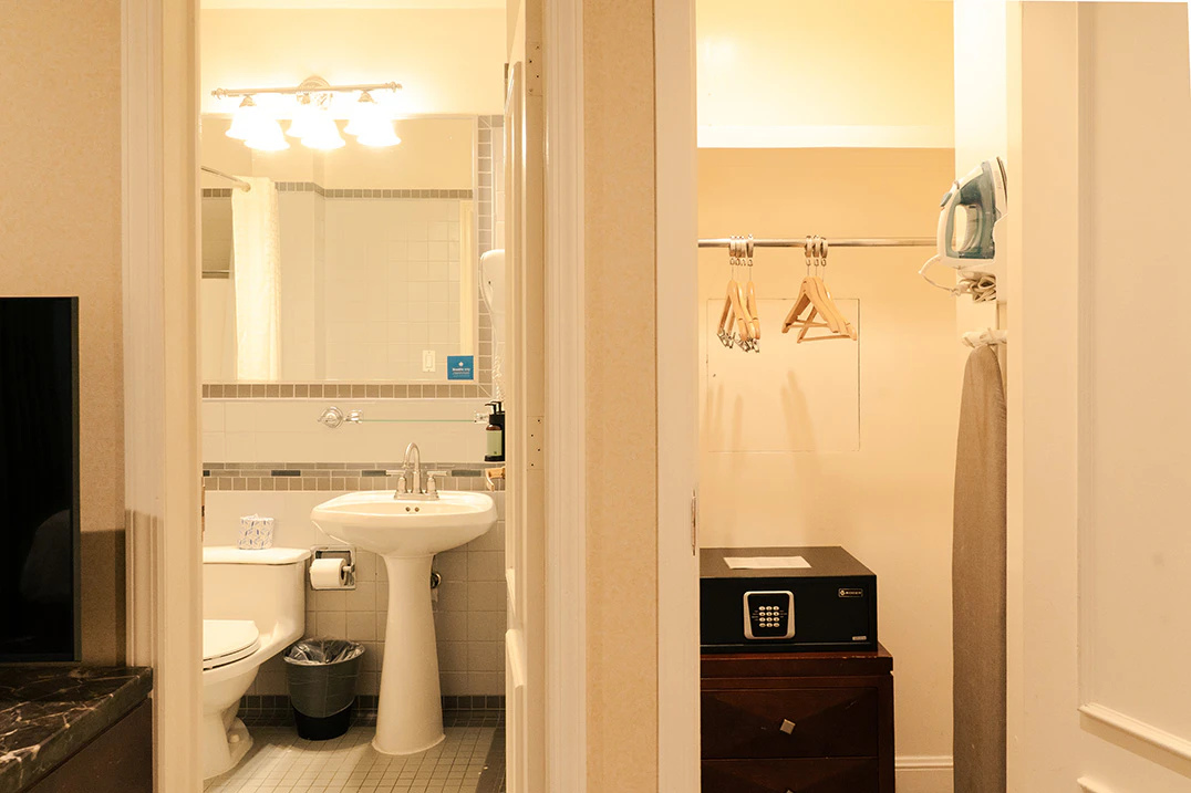 A bathroom with a toilet, pedestal sink, and closet with an iron and safe