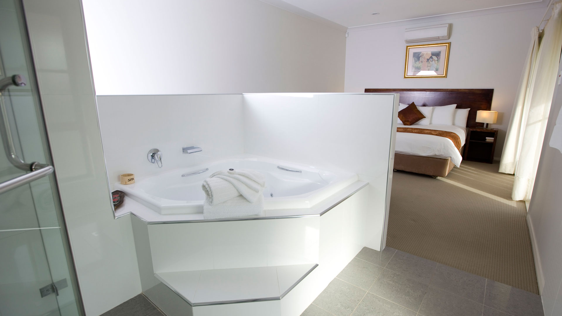 Luxury ensuite at Talga Estate featuring a two-person corner spa bath with chrome fittings, open to the king bedroom