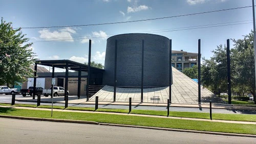 The exterior of a modern building with a curved facade and pyramidal base.
