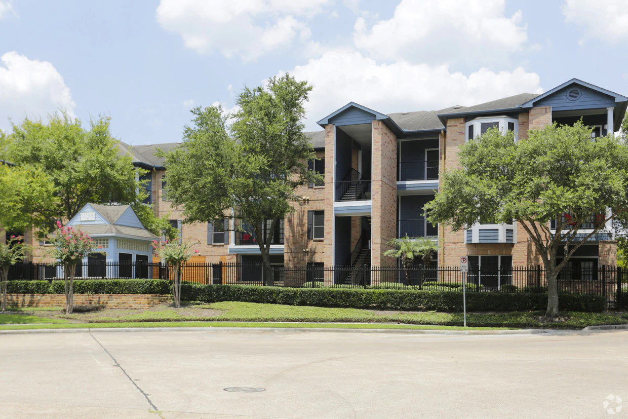 A three-story brick building with balconies and a fenced-in front yard.
