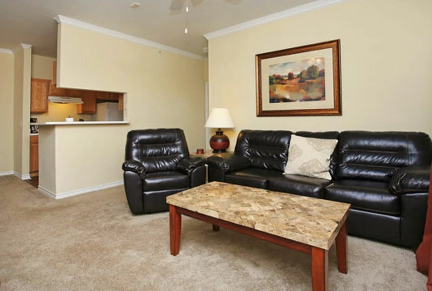 A living room with a black leather sofa, armchair, coffee table, and painting on the wall.