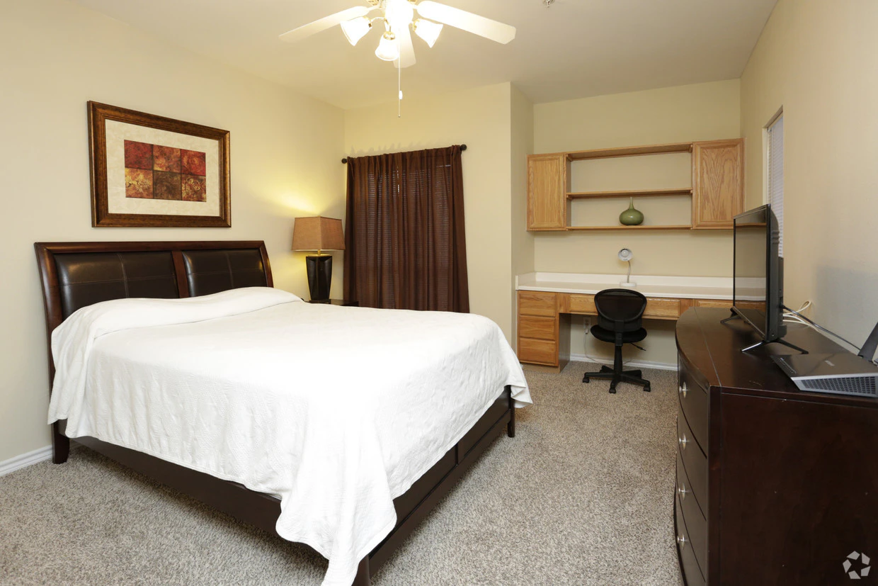 A hotel room with a bed, desk, TV, and ceiling fan.