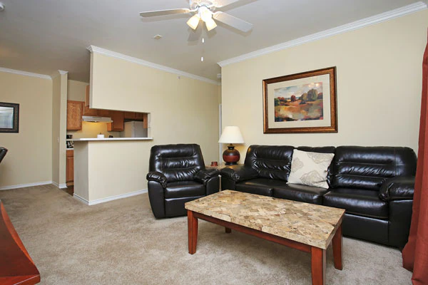 A wide-angle view of a living room with a sofa, recliner, coffee table, and kitchenette.