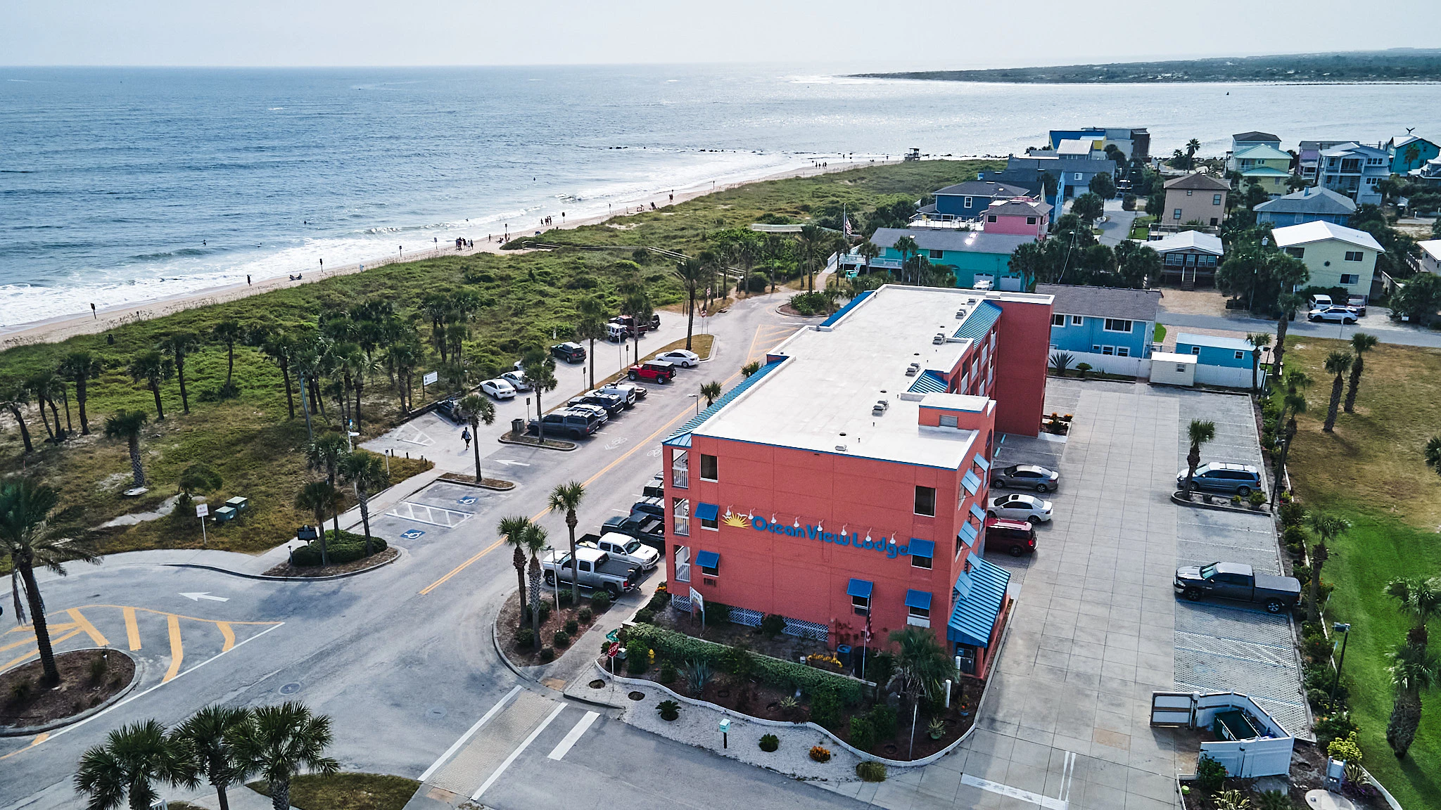 Aerial view of a beachfront hotel with a parking lot and palm trees.