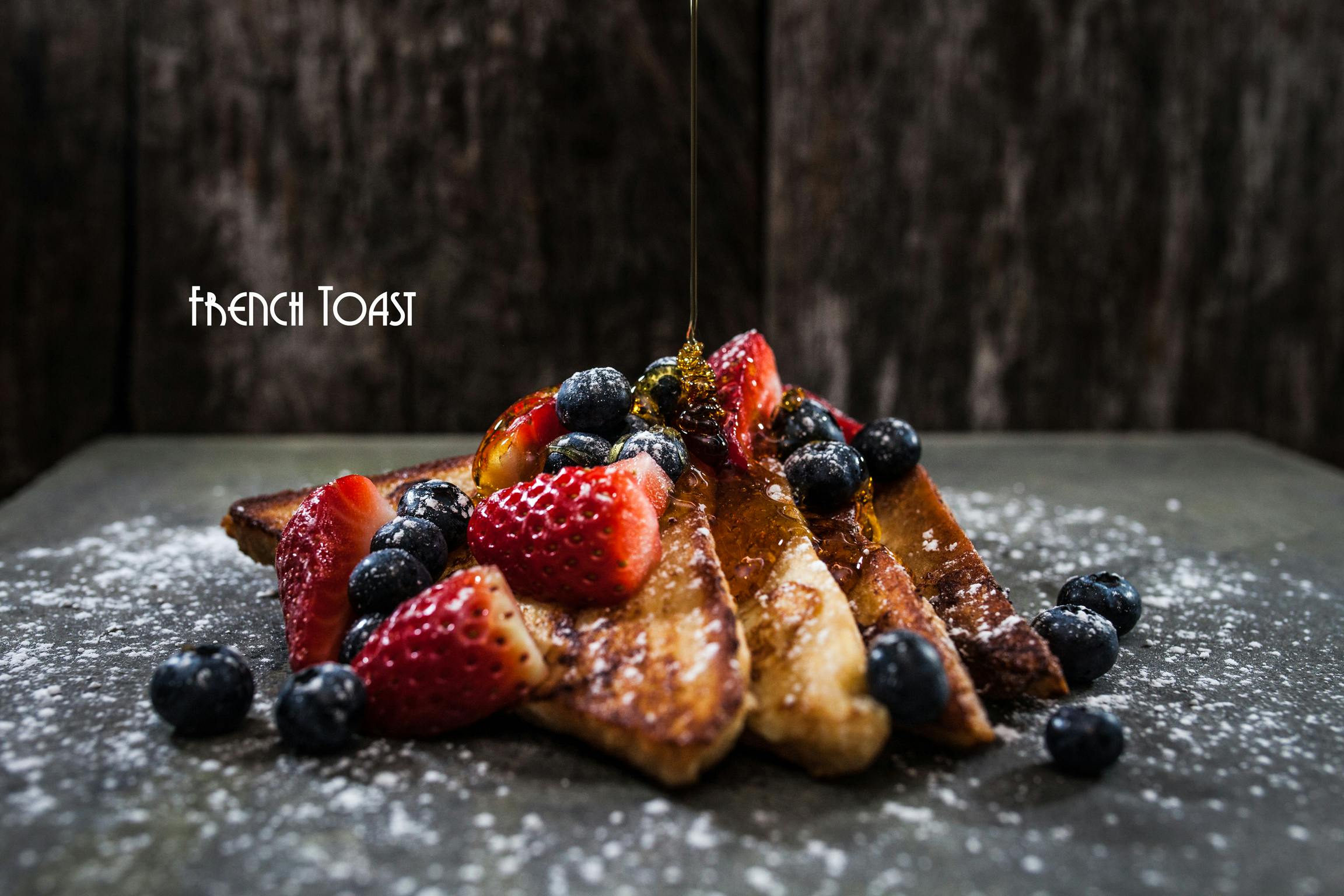 four pieces of fresh prepared french toast with a mix of fresh fruits and maple syrup, coated by icing sugar